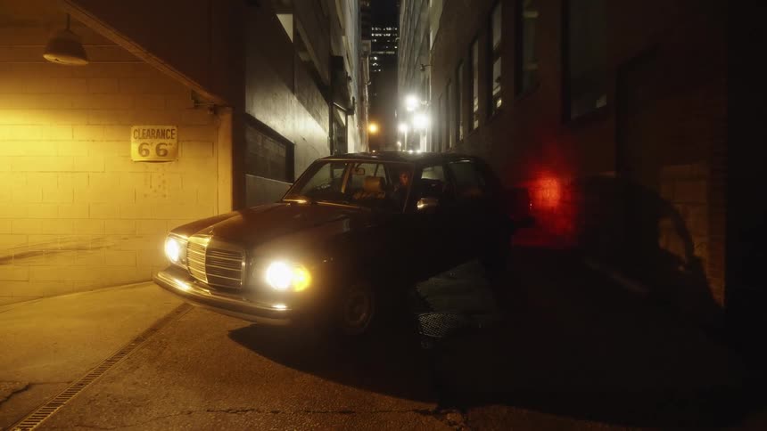 Man parked in a car at night thinking deeply in a city alley