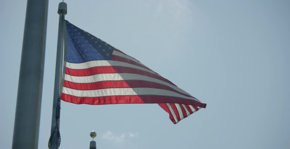 American flag swaying from flag pole on a breezy blue sky day
