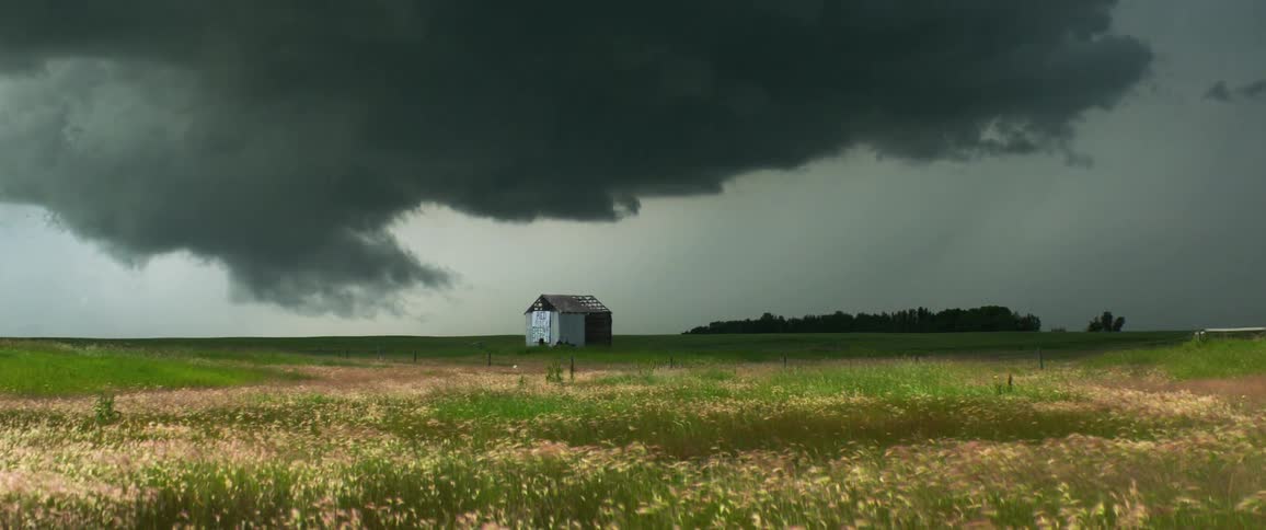 A dark storm cloud hovers over a diminished shack in the country