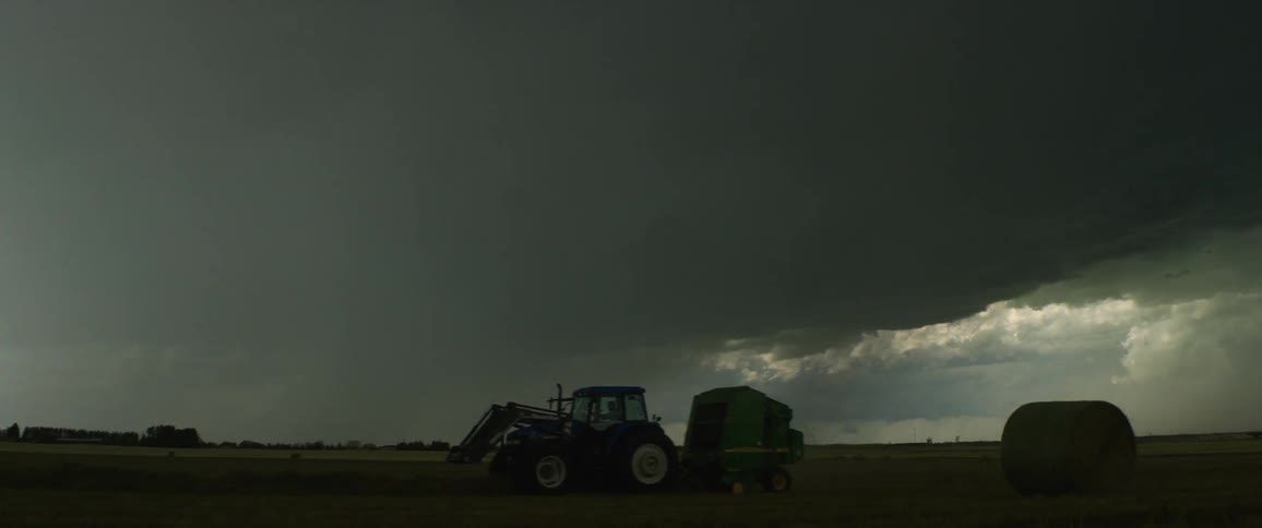Dark clouds over a field as a tractor drives across it