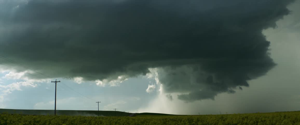 Above a wide open field lingers a large dark cloud that threatens rain looks