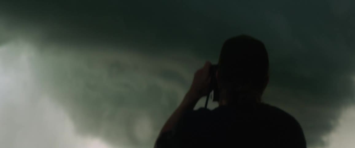 A man stands before an ominous looking storm cloud while attempting to photograph it