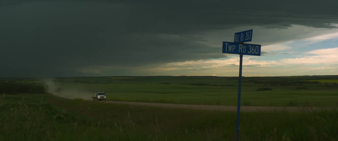 A truck with cargo driving on a rural dirt road with storm clouds floating overhead