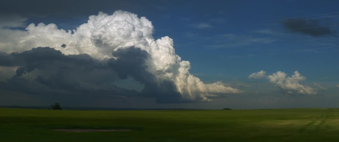A few metal silos sit amidst sprawling open farmlands under large fluffy clouds