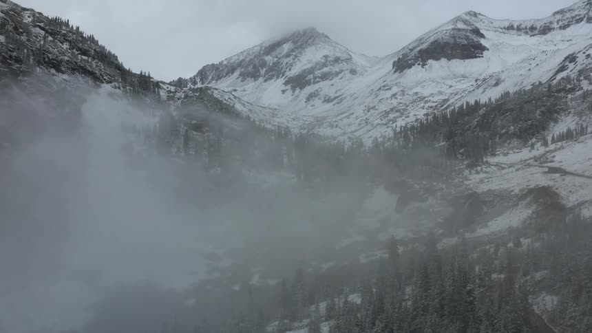 Fog obscures parts of snow covered mountains and conifer forest