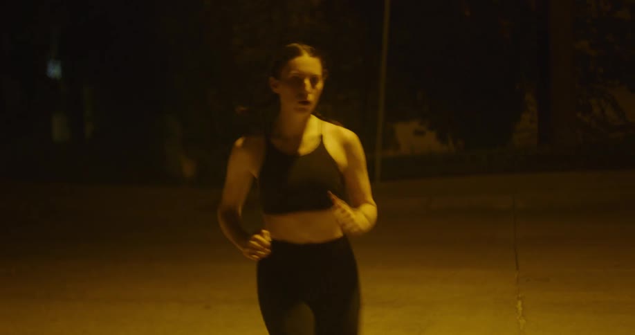 A young woman jogs along a paved area outdoors at night