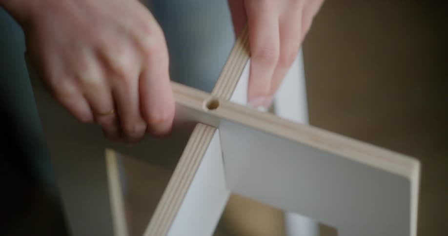 Woman assembes a wooden stand in a room at home