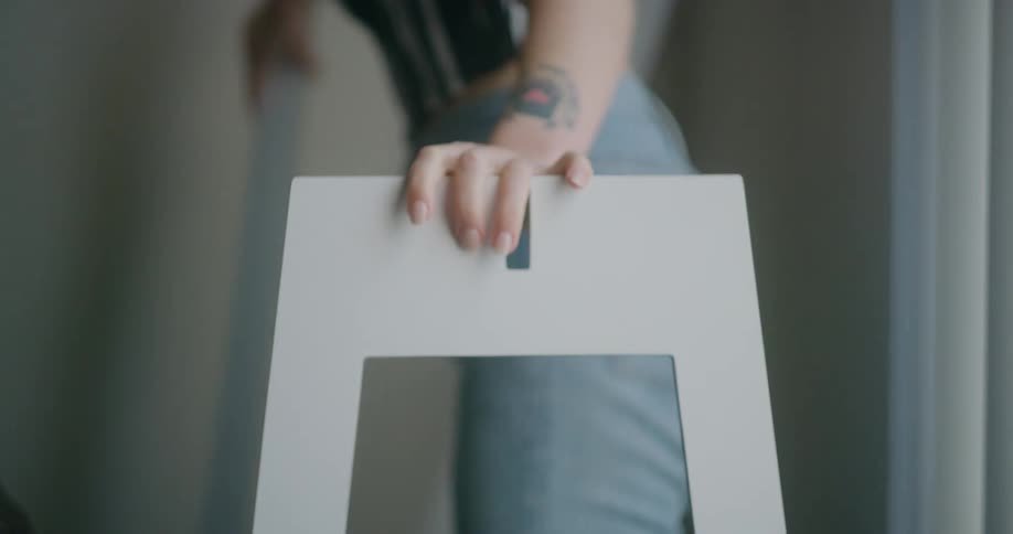 A woman walks into a room and puts together two white pieces of furniture