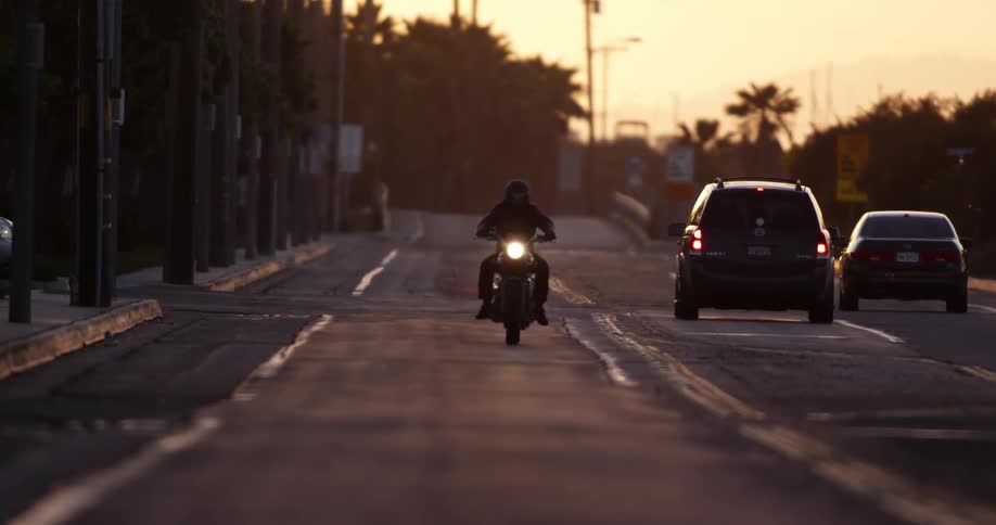 A person with a helmet riding a motorcycle on a road with vehicles with the sky and clouds in the background
