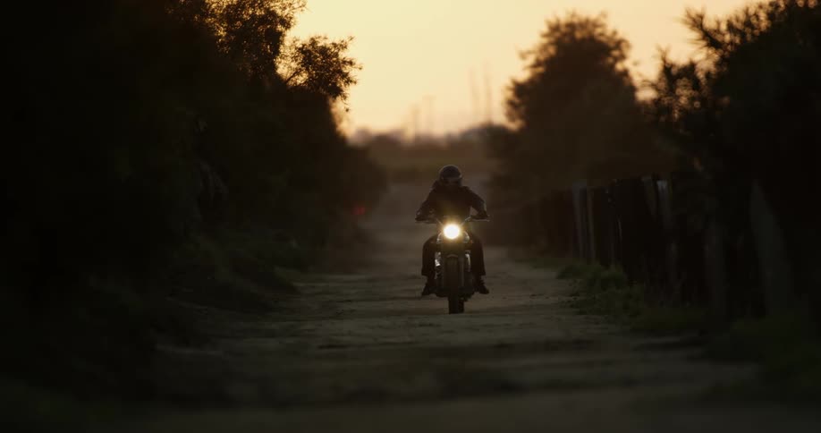 Person riding motorcycle with headlight on rides down the road at dusk