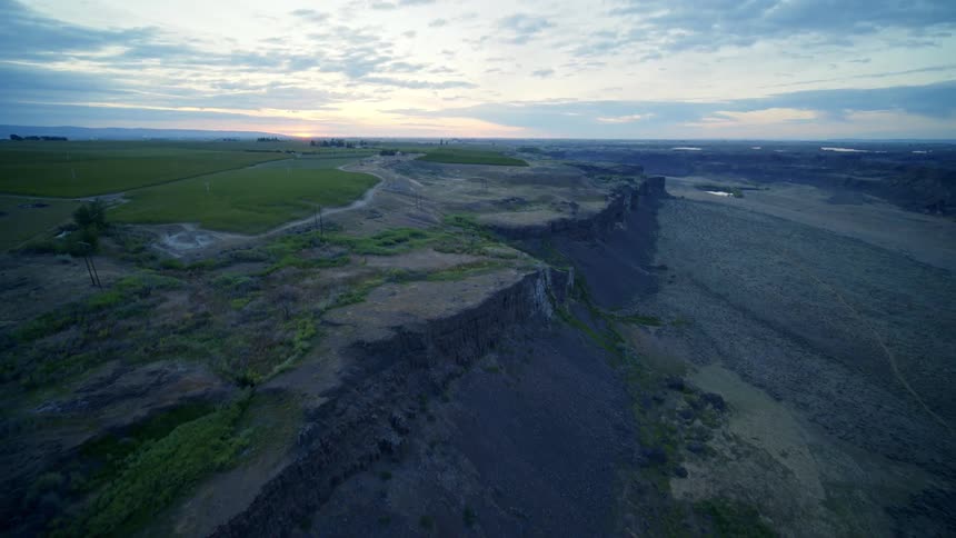Green irrigated farm fields extend close to the edge of an arid canyon valley cliff