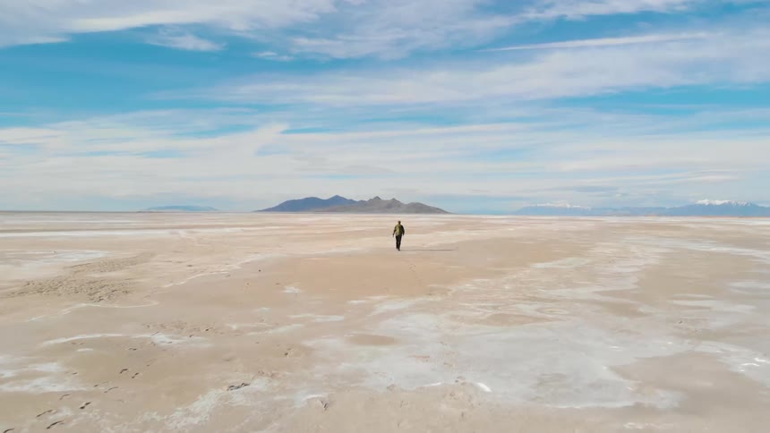 A man hikes alone through a vast desert toward a canyon in the distance