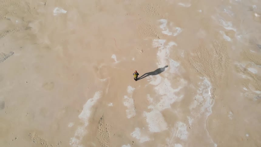 Man walking across beach casting a shadow upon the sand