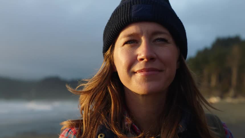 A female caucasian standing on a beach near a wooded area