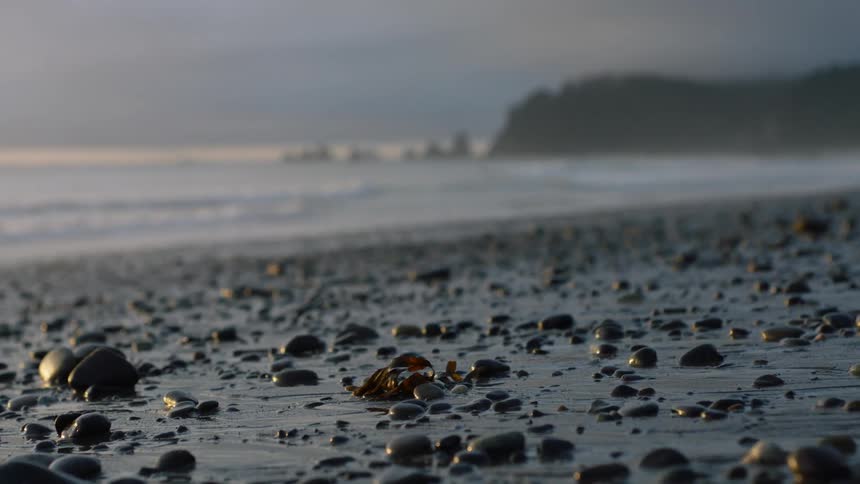 A beach with sand and stones with the sky and clouds in the background