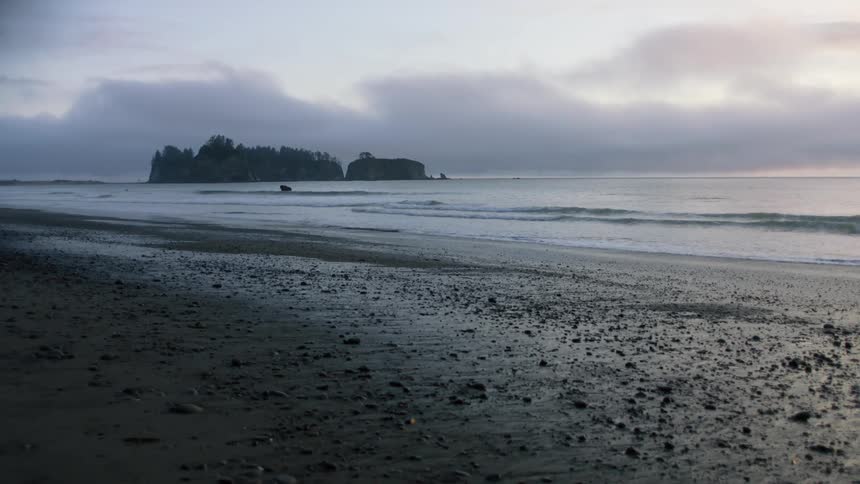 Forest covered small islands sit just off beach under cloudy sky with pink tinted horizon