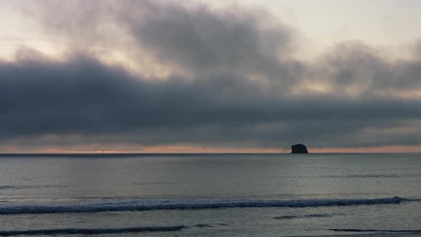 Low waves roll into a beach under a cloudy sky in the evening