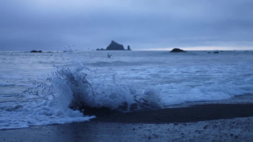 Ocean waves wash over a stone on a beach on a cloudy evening