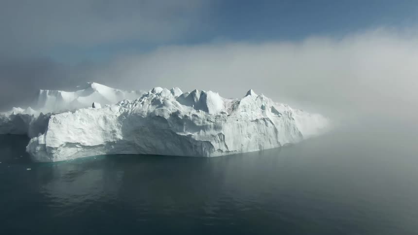 Iceberg floats in water among clouds