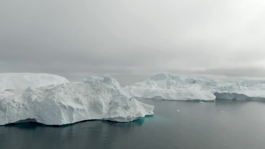 Large glaciers float float atop the ocean water under a cloudy sky