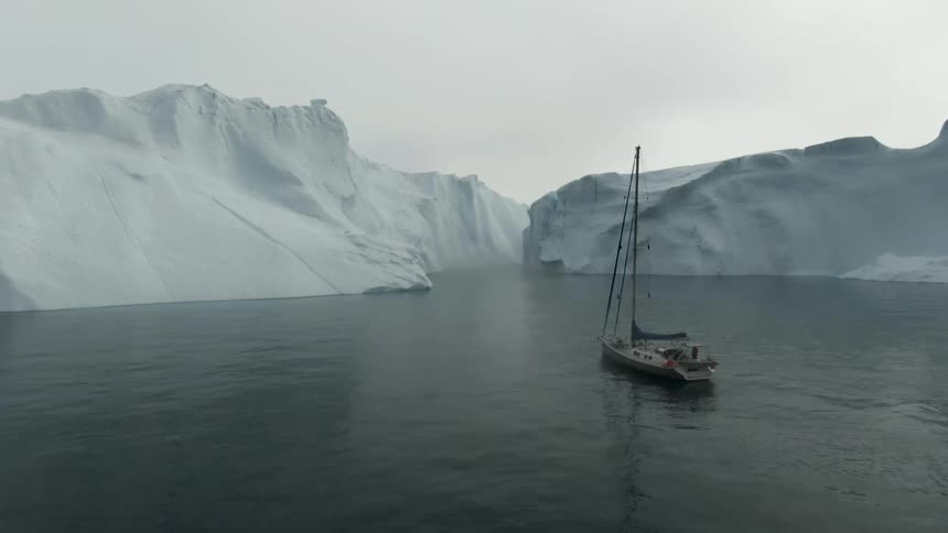 A small sailboat is anchored in the ocean near a large snow cap
