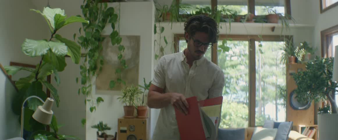Man standing in a living room unpacking a box and reading from a folder