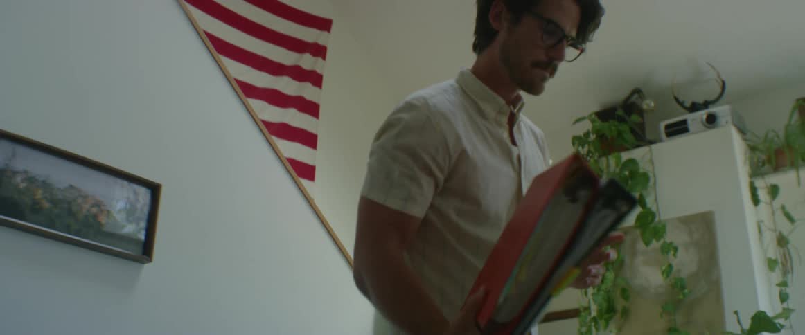 Man inside a home picking up folders from off of the ground to take them over to sofa to read
