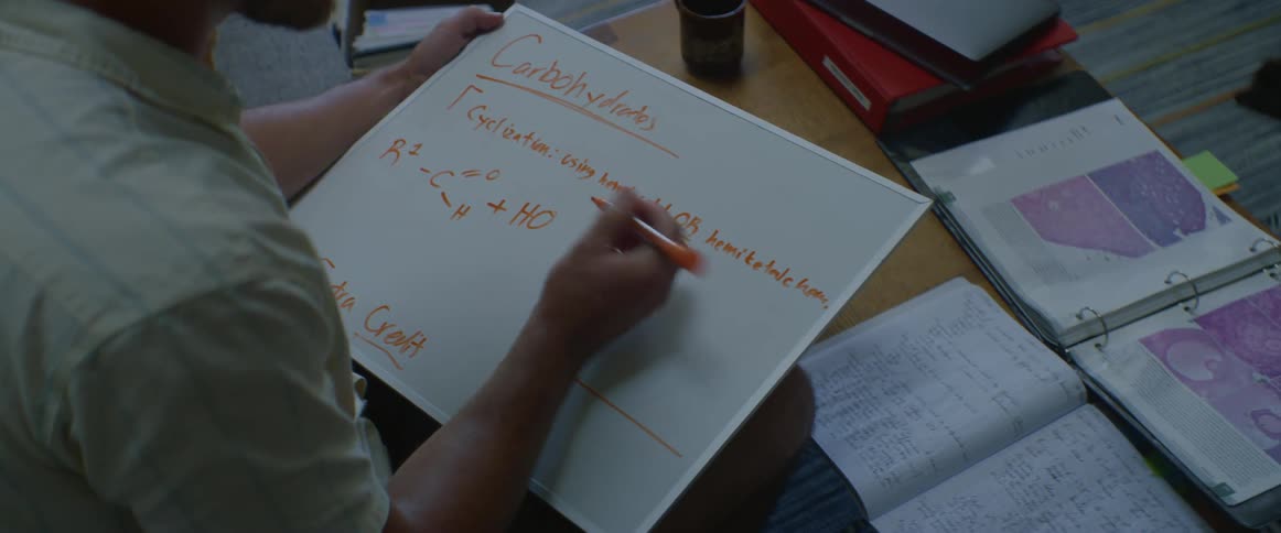 Man sitting down inside solving chemistry problems on a white board