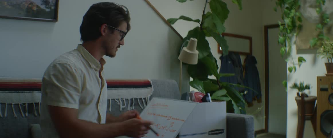 A man appears to be talking with someone and holds up a whiteboard with writing on it
