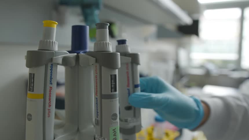 Hand spins a small carousel with medical equipment in a lab and picks a test tube from rack