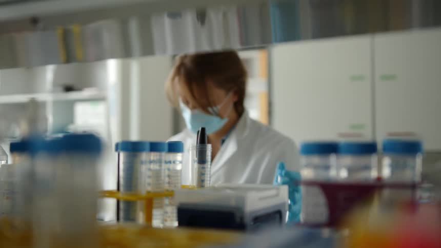 A woman in a lab sets a tray of test tubes on a shelf and removes one