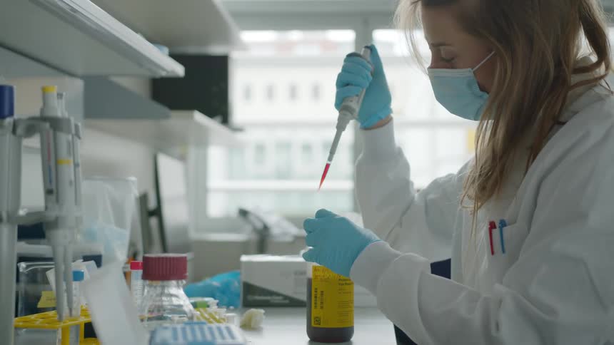A female lab technician extracts a sample from a bottle and goes to deposit it into a test tube