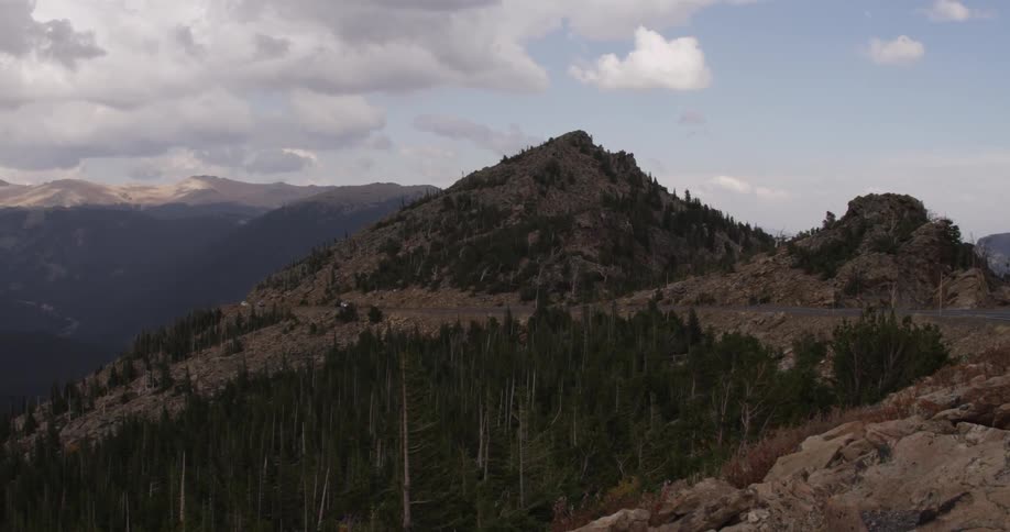 Far off in the distance vehicles travel on a road running through hills with pine trees
