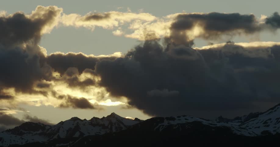 Dark clouds lit up by sunlight move over a mountain range