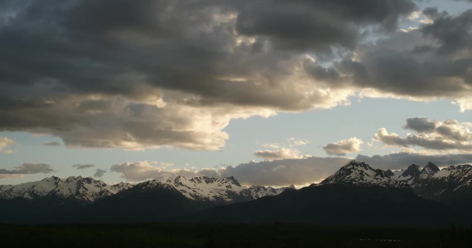 Dense and fluffy clouds float over snow covered mountains