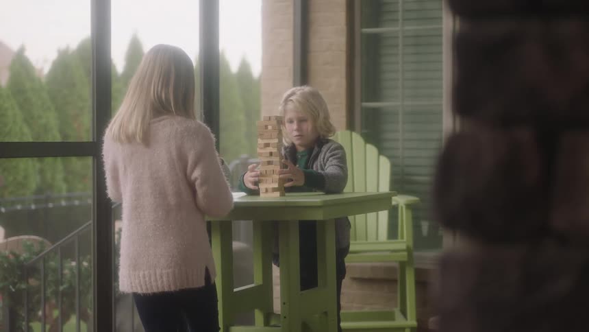 Three children are at a table on a balcony playing a game on a table