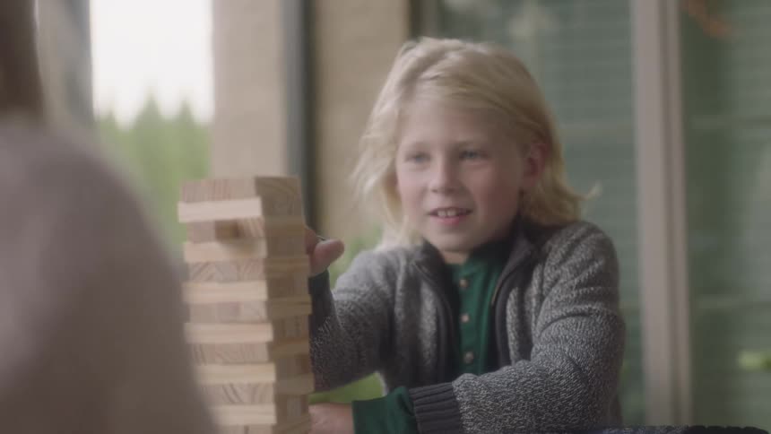 Young boy sitting down at a table inside playing a table top game with wooden blocks