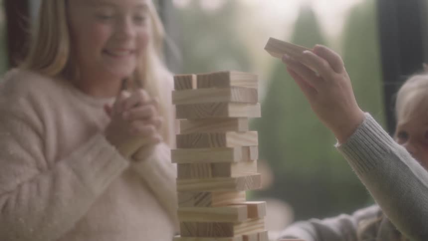 Siblings sitting at a table inside playing a table game with wooden blocks