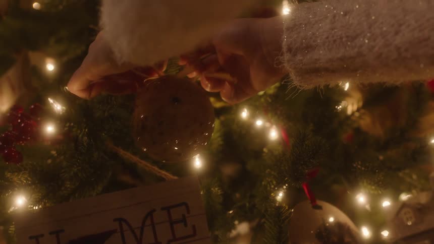 A woman in a sweater is carefully placing an ornament on a christmas tree