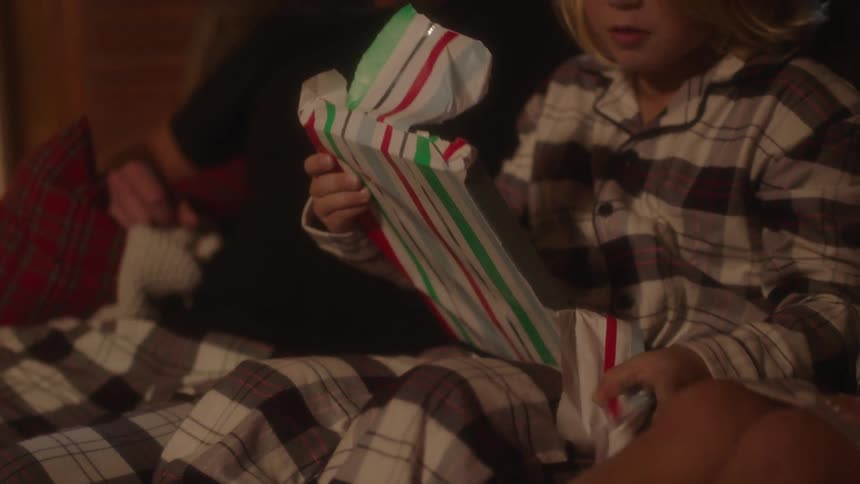 A boy sitting on a couch unwrapping a gift