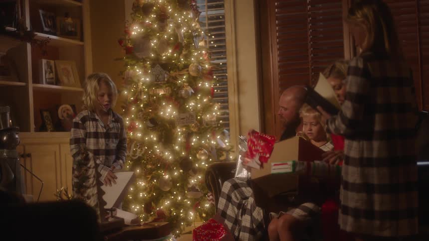 Family sitting in a living room opening presents around a christmas tree