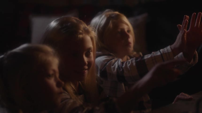 A group of three blonde girls wearing pajamas sitting in front of a fireplace in a dimly lit room
