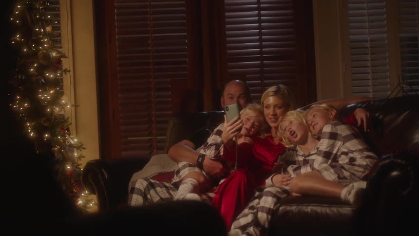 A family poses together on a sofa as the mother holds a smartphone to take a selfie