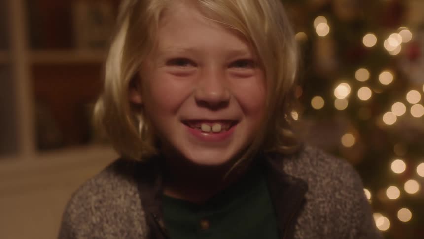 Boy standing in front of a christmas tree laugh and smiling
