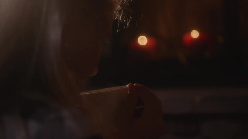 A woman sips tea next to burning candles