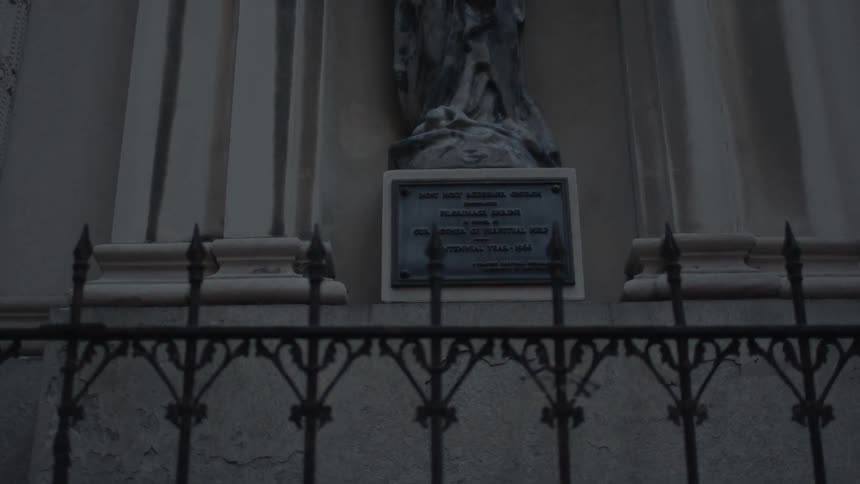 A statue with a plaque behind an iron gate