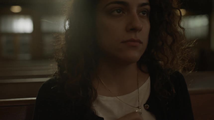 A woman is sitting in a pew holding her necklace