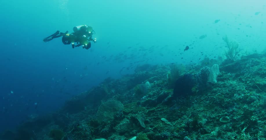 A diver films the sea floor with an underwater camera while using an underwater scooter for propulsion