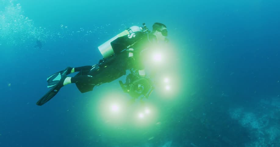 Man holding a camera scuba diving in the ocean