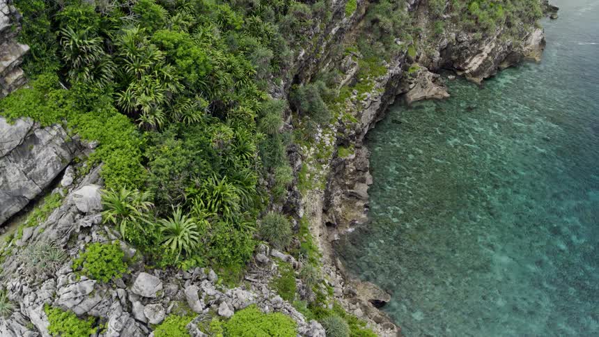 An aerial view of turquoise ocean water flowing towards a rocky tropical island